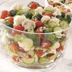 a glass bowl filled with lots of veggies and cauliflower on top of a table