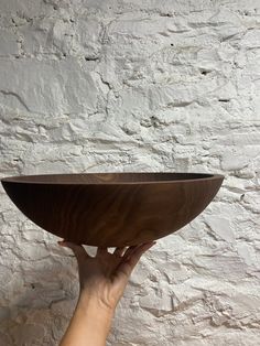 a person holding a wooden bowl in front of a white brick wall