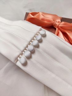 a white dress with orange ribbon and buttons on the front, sitting on a bed