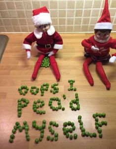 two elfs sitting on top of a wooden table next to green peas and the words i love santa spelled by them