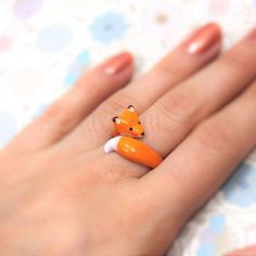 a woman's hand with an orange fox ring on it