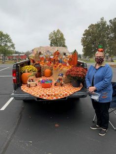 a woman standing next to a truck filled with pumpkins and other fall decorating items