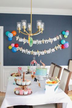 a birthday party with cake, cupcakes and balloons hanging from the ceiling over a dining room table