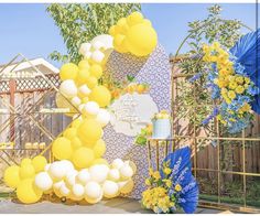 an outdoor party with yellow and white balloons, blue decorations and flowers on the table