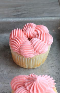 two cupcakes with pink frosting sitting on top of a metal tray next to each other