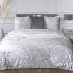 a bed with silver sheets and pillows on top of it in a white walled room