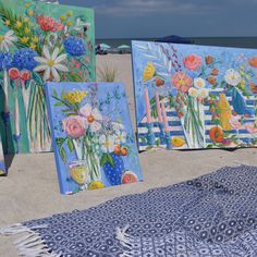 four paintings on the beach with flowers in vases and blue sky behind them,