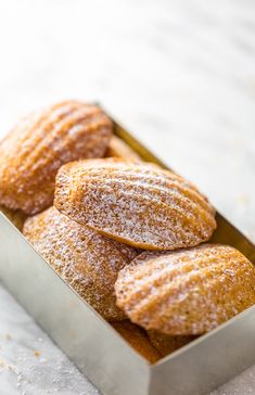 powdered sugar covered doughnuts in a metal box on a white tablecloth