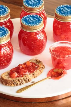 several jars of jelly sit on a plate with bread and jam in the foreground