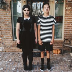 two children dressed up in halloween costumes standing on a brick walkway with pumpkins behind them