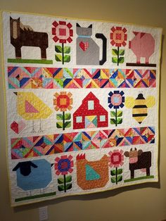 a quilt hanging on the wall with farm animals and flowers in it's center