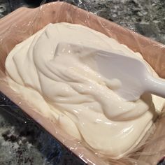 a plastic container filled with white icing on top of a counter next to a wooden spoon