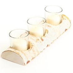 three candles are sitting on a piece of wood that is holding two glass holders with one candle