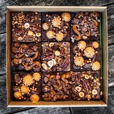 a box filled with brownies covered in nuts and other toppings on top of a wooden table