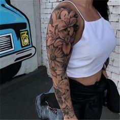 a woman with a flower tattoo on her arm is walking down the street in front of a brick wall