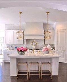 a white kitchen with gold accents and pink flowers on the countertop, along with two stools