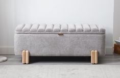 an upholstered bench with wooden legs in front of a white wall and floor