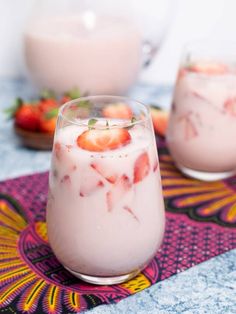 two glasses filled with yogurt and strawberries on top of a tablecloth