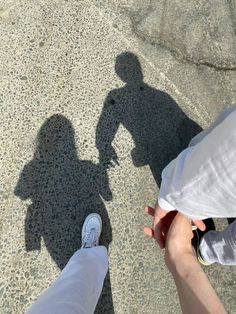 two people standing next to each other with their shadows on the ground and one person holding his hand