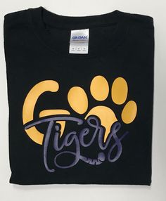 Go Tigers vinyl shirt. Mascot name can be changed to fit your needs. Shirt style may vary depending on availability. Available in adult sizes upon request. Vinyl can be done in a different color. Please leave me a note for any color changes. Made in a smoke free and pet free home. Thank you for visiting my shop! Have a blessed day! Black School Spirit T-shirt With Screen Print, Sporty Black Tops With Heat Transfer Vinyl, Graphic Tee Shirt With Heat Transfer Vinyl For Fans, Black T-shirt With Heat Transfer Vinyl For School, Black Shirt With Letter Print For Fans, Black Cotton Screen Print Transfers, Black Screen Print T-shirt For School, Black T-shirt With Screen Print For School, Black Custom Print Shirt For College