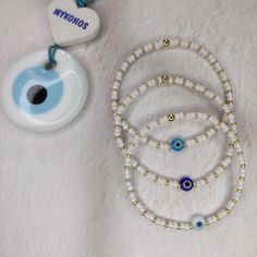 three bracelets with evil eye charms and a pacifier on a white surface next to it