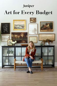 a woman sitting on top of a wooden bench in front of a wall filled with pictures