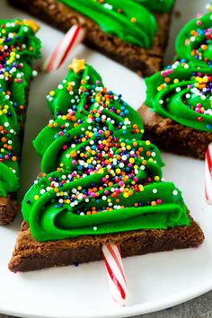 green frosted christmas tree cookies on a white plate with candy canes and sprinkles