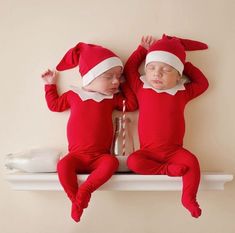 two babies dressed in red and white are laying on a shelf next to each other