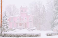 a pink house is covered in snow with trees and bushes on the other side,