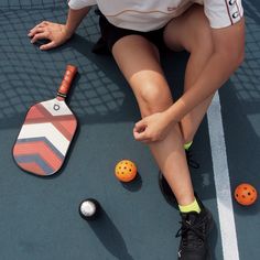 a woman sitting on the ground next to tennis balls and racquets,