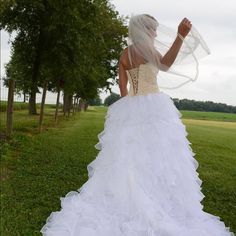 a woman in a white wedding dress is standing on the grass with her veil over her head