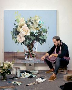 a man sitting in front of a painting with flowers on the ground next to it