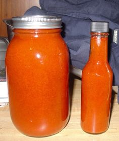 two jars filled with orange colored liquid sitting on top of a wooden table next to a blue bag