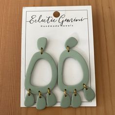 two pairs of green and gold earrings on top of a wooden table next to a card