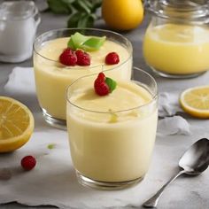 two glasses filled with pudding sitting on top of a table next to lemons and raspberries