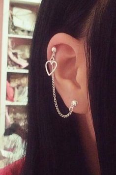 a woman with long black hair wearing a heart and chain earring set in front of her ear