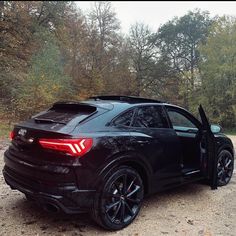 a black car parked on top of a dirt road next to trees in the woods