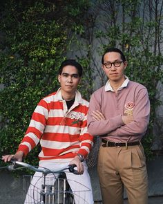 two men standing next to each other with their arms crossed and one on the bike