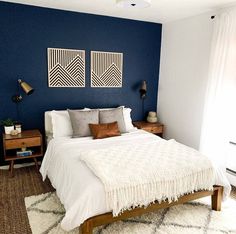 a bedroom with blue walls, white bedding and two pictures on the wall above it