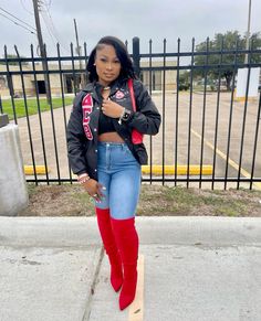 a woman standing on the sidewalk with her arms crossed wearing red boots and a black jacket