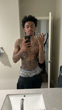 a man with tattoos taking a selfie in front of a mirror while holding a cell phone