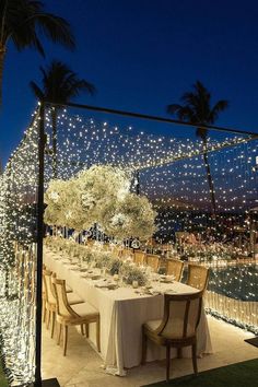 an outdoor dining table set up with lights on the ceiling and palm trees in the background