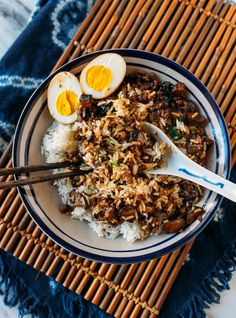 a bowl filled with rice, eggs and meat on top of a bamboo place mat