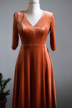 an orange dress is on a mannequin with a potted plant in the background