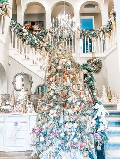 a decorated christmas tree in the middle of a room with stairs and chandelier