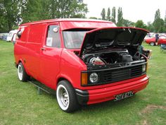 an orange van parked next to other cars on a grass covered field at a car show