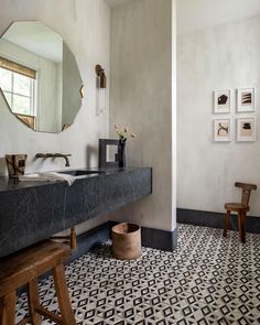 a bathroom with a black and white tile floor, mirror, stools and pictures on the wall