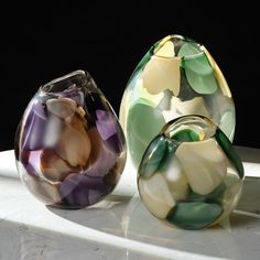 three glass vases sitting on top of a white table next to each other in different colors