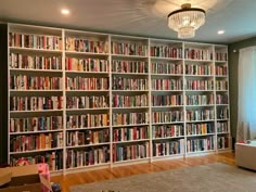 a living room filled with lots of books on top of a white book shelf next to a window