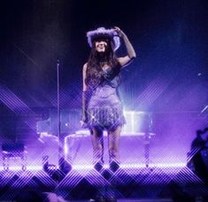 a woman standing on top of a stage wearing a purple dress and feathered hat